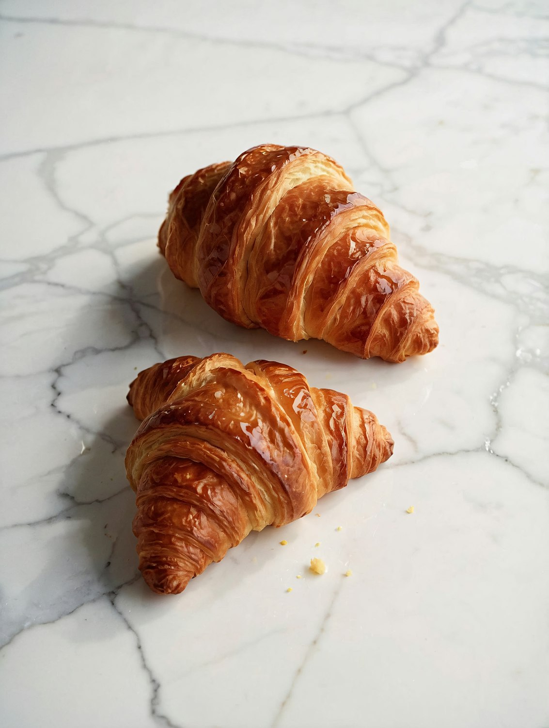 Two golden butter croissants on a marble surface